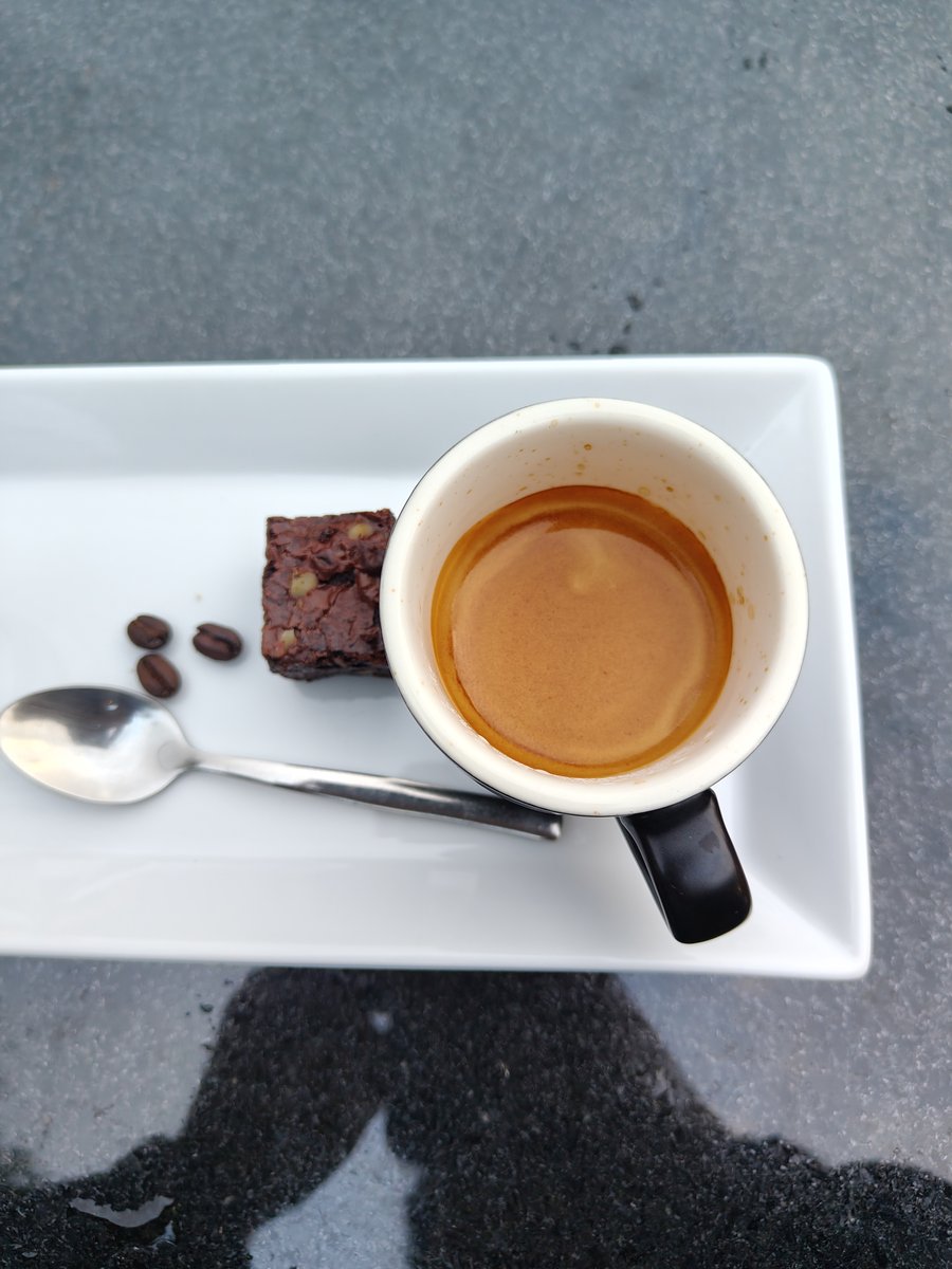 Een kop espresso met een klein chocoladedessert en een lepel op een wit bord.