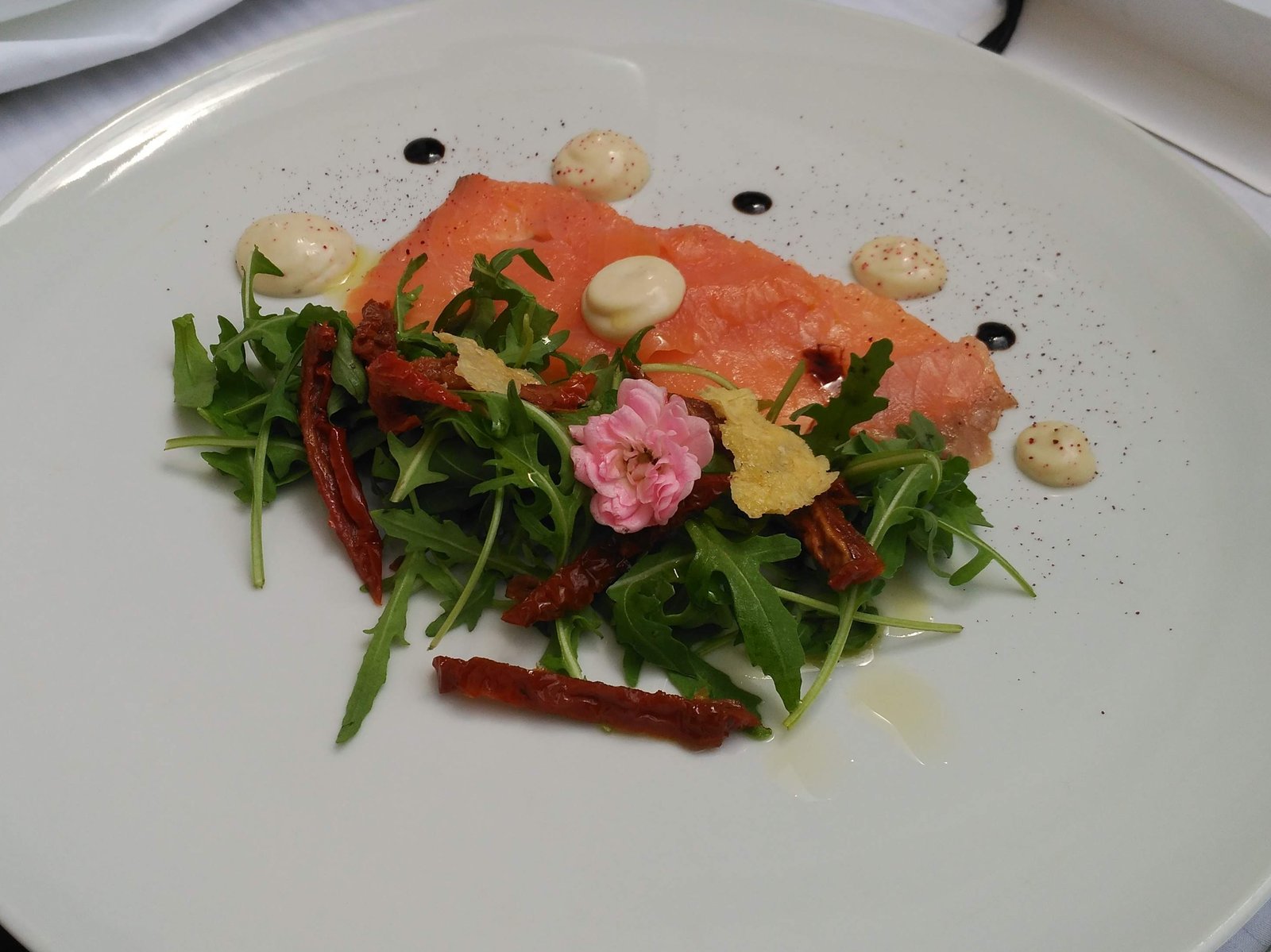 Een restaurantbord met plakken zalm, groene salade en kleine hoeveelheden saus.
